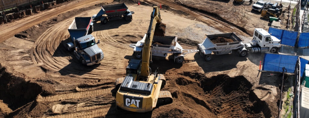 Excavator and haul trucks performing earthwork and site excavation