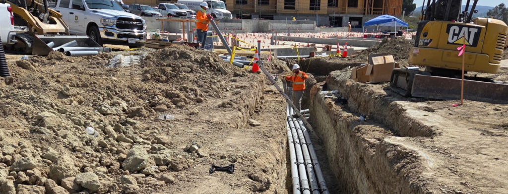 Underground utility trench with construction crew installing conduit and pipe systems