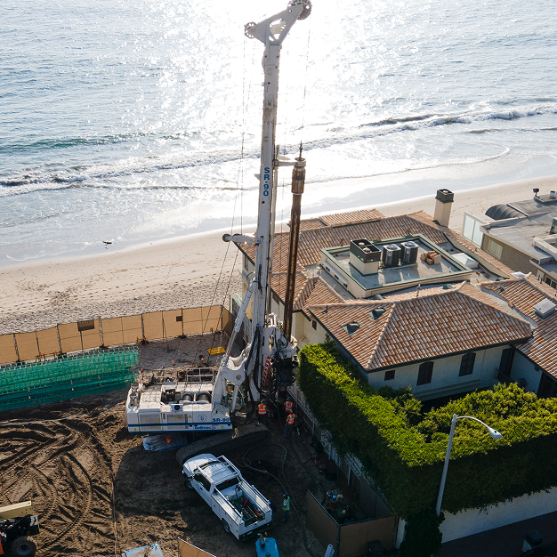 Deep foundation drilling rig operating beside coastal residential development