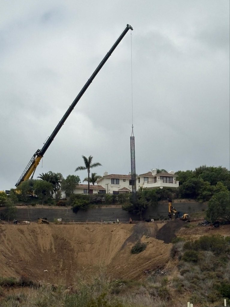 A crane sets a rebar cage over the slope.